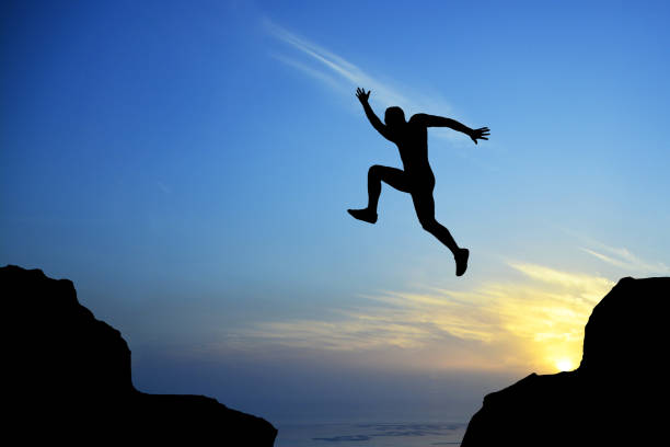 istock Man silhouette leaping on cliff on sunrise, success concept 1085265418