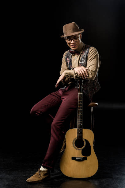 istock handsome man in stylish hat posing with acoustic guitar while sitting on chair on black 1085268290