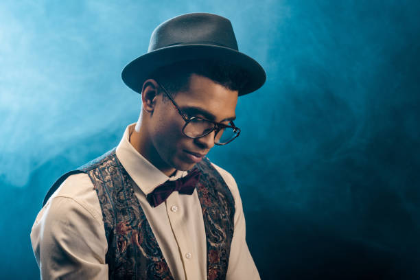 istock mixed race young man in stylish hat and eyeglasses posing on stage with smoke and dramatic lighting 1085268314