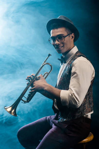 istock happy young jazzman posing with trumpet on stage with dramatic lighting and smoke 1085268330