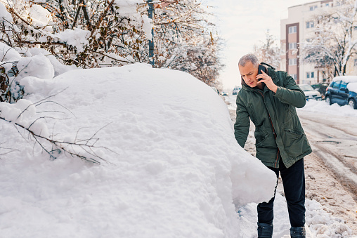 Photo of mature Man using smartphone and calling for help because his car is broken. road problems. Gray hair male using smartphone to call road assistance. Snow, Winter and vehicle concept.