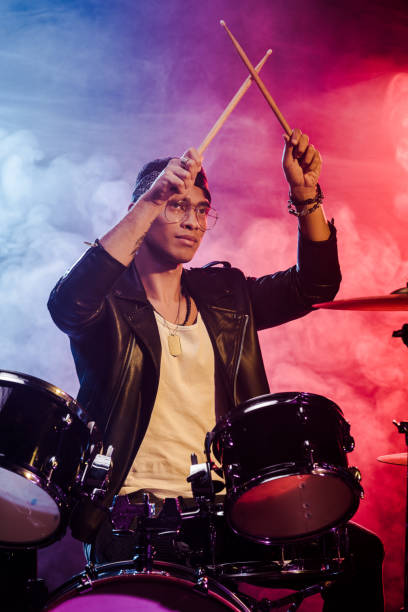 istock mixed race male musician raising drum sticks while sitting behind drum set on stage with dramatic lighting and smoke 1085273870