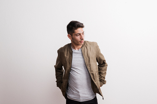 A confident young hispanic man with jacket in a studio, hands in pockets.
