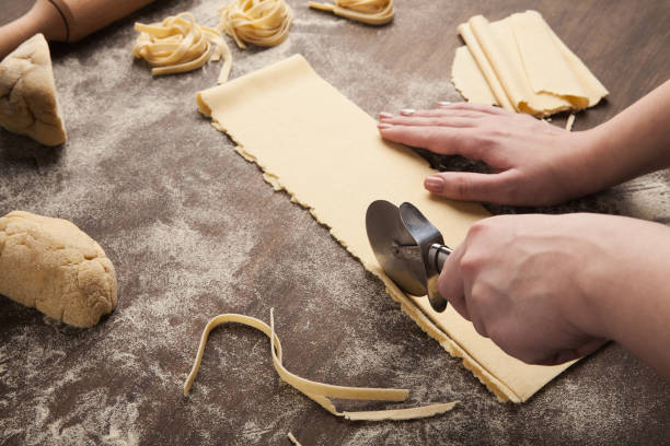 Chef using wheel cutter in preparation of pasta Cutting raw dough. Chef using wheel cutter in preparation of italian pasta on kitchen table, copy space dough cutter stock pictures, royalty-free photos & images