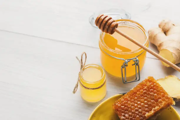 Fresh honeycombs, honey in jar and fresh ginger on white wooden background, natural medicine concept, copy space