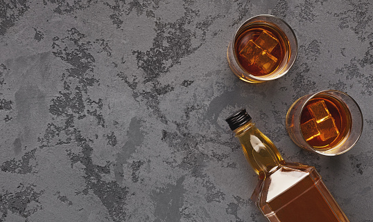 Two glasses of whiskey and bottle aside on marble background, top view, copy space