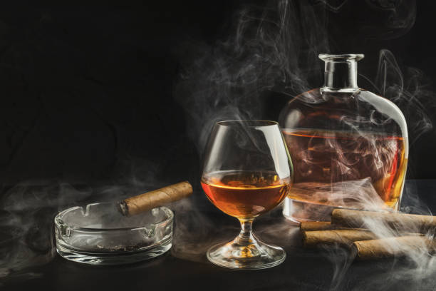 bicchiere di whisky con sigaro fumante e bottiglia - cigar whisky bar cognac foto e immagini stock