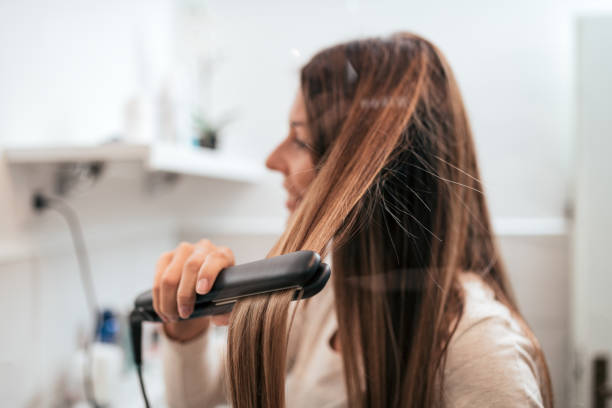 Young woman straightening her hair in the bathroom. Young woman straightening her hair in the bathroom. adjusting stock pictures, royalty-free photos & images