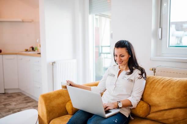 istock Smiling young woman using laptop while sitting on sofa at home. 1085333394