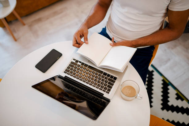 istock Man working at home. Blank open book, laptop, smart phone and coffee on table. Top view. 1085333642