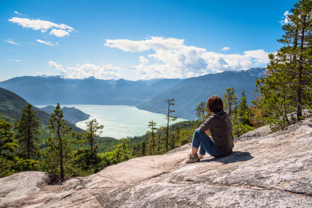 mujer sentada sobre una roca en la cima de una montaña admirando el espectacular paisaje en un día soleado de verano - landscape canada mountain rock fotografías e imágenes de stock