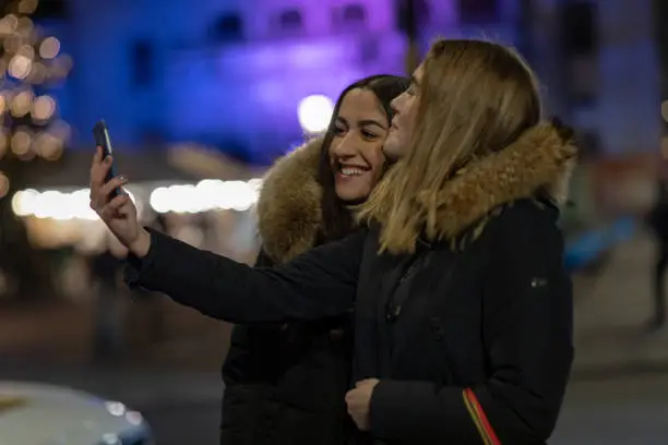 Two young women are taking a selfie on their smartphone in Gothenburg city. They are holding shopping bags.