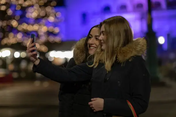 Two young women are taking a selfie on their smartphone in Gothenburg city. They are holding shopping bags.