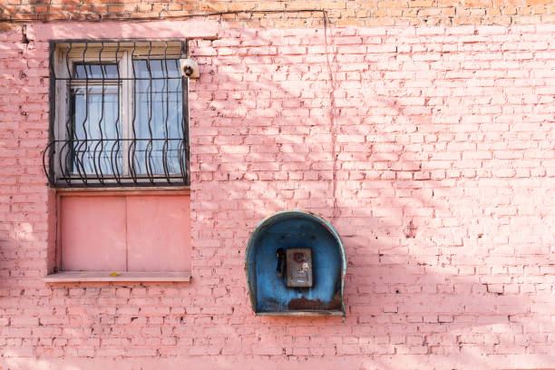 vieux téléphone cassé de la période soviétique sur le mur de briques roses de la maison et la fenêtre - pay phone brick wall telephone old photos et images de collection
