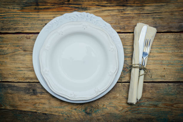 istock Empty white rustic plate on old wooden background with knife, fork and napkin. Rustic food concept. Copy space 1085380360