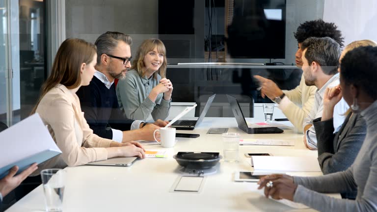 Panning shot of business people discussing over document in office. Male and female professionals are working on new project. They are sitting at conference table.