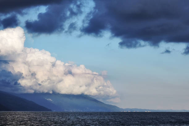 Pyrocumulative and thunderstorm clouds, partially illuminated by the sun, over the mountains and the sea