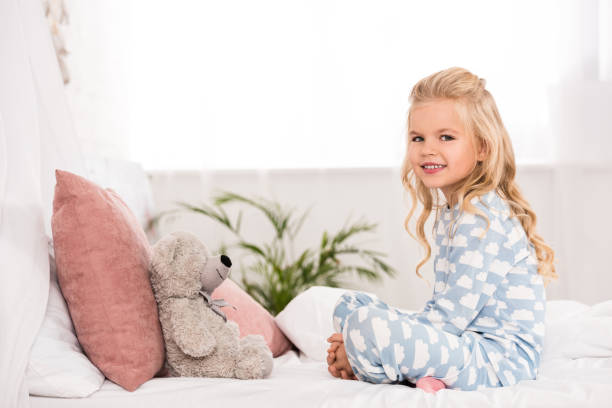 istock cute child sitting on bed with crossed legs and teddy bear 1085391506