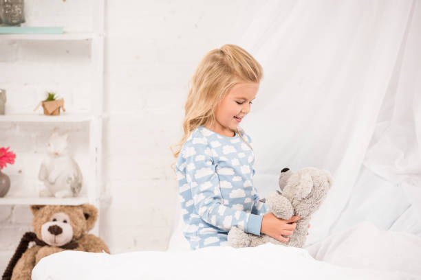 istock cheerful kid playing with teddy bear in bed 1085391622