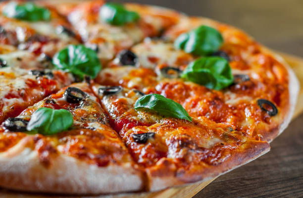 istock sliced Pizza with Mozzarella cheese, Tomatoes, pepper, olive, Spices and Fresh Basil. Italian pizza. Pizza Margherita or Margarita on wooden table background 1085393330