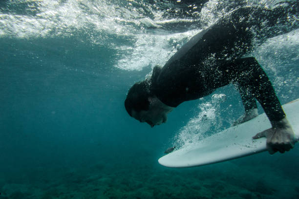 istock Man in the black swimsuit holding a surf board dive under the wave 1085395016