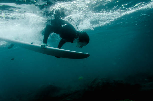 istock Man in the black swimsuit flowing down holding a surf board dive under the wave 1085398260