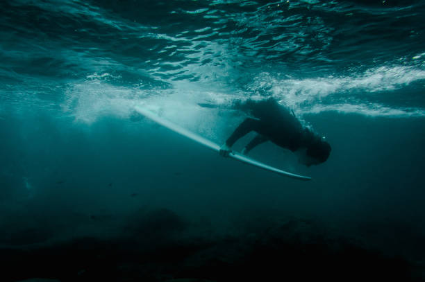istock Boy in the black swimsuit flowing down holding a surf board dive under the wave 1085398366