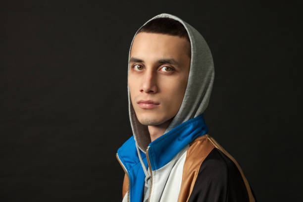 A high contrast image of a young man in a hooded sweatshirt in front of a wall covered in graffiti.