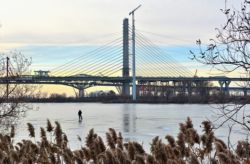 Lifestyle...This wide shot, shows a man fishing patiently, on cold, early morning, the new Champlain Bridge, still under construction, stands behind him. This image was taken on the St. Lawrence River at Montreal, late December 2018.