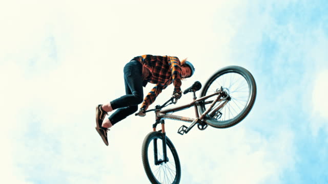 MS Young man spinning with BMX bicycle against cloudy sky