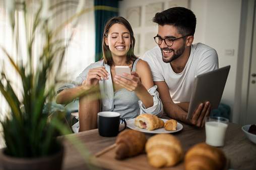 Young couple at home using tablet and smartphone - Morning breakfast time