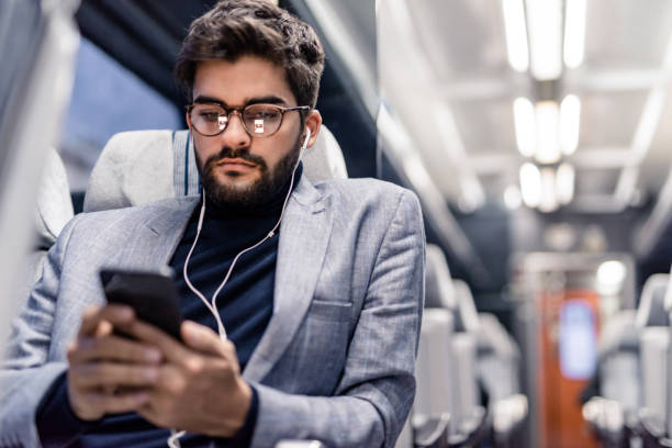 Young man reading an article on his phone and listening to podcasts while traveling by train. Young man reading an article on his phone and listening to podcasts while traveling by train. podcasting photos stock pictures, royalty-free photos & images