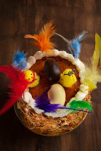 Closeup of a mona de pascua, a cake eaten in Spain on Easter Monday, ornamented with feathers and a teddy chick on on a rustic wooden surface. Vertical.
