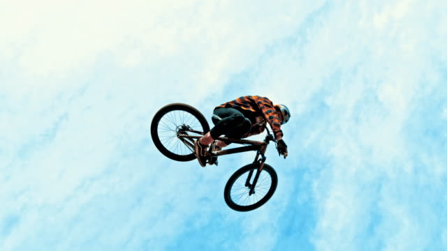 MS Young man jumping BMX bicycle against blue sky and clouds