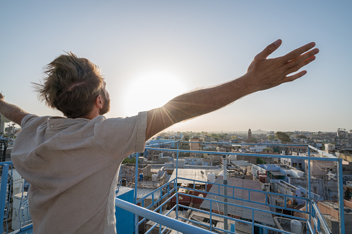 Happy man arms outstretched at sunrise in Jodhpur city from rooftop, India