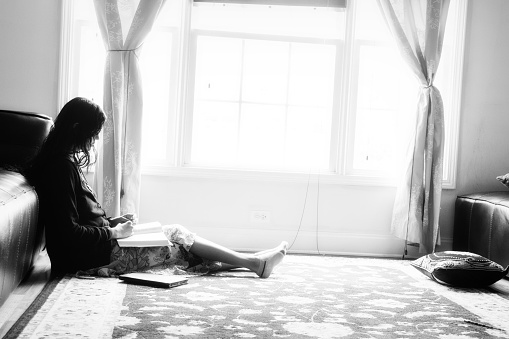 An Indian woman reading a book by sitting near a window