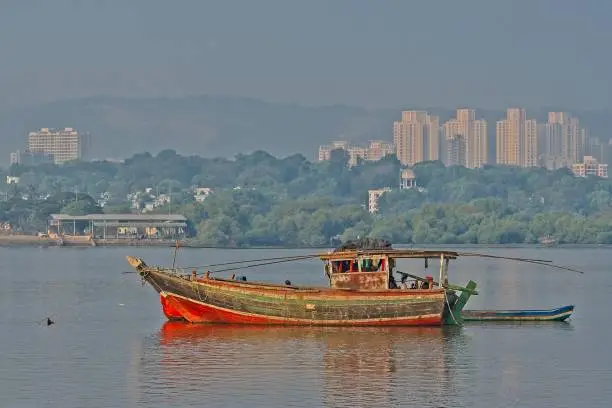 Effect of urbanization where one can see an a dilapidated boat at the Thane Creek against backdrop of tall buildings in Thane Creek