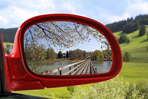 Landscape reflected in the rear view mirror of a red car - spring series