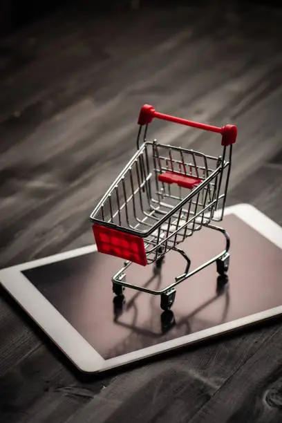 close-up of shopping trolley on tablet with darkwood background with some copy space,shopping online concept.