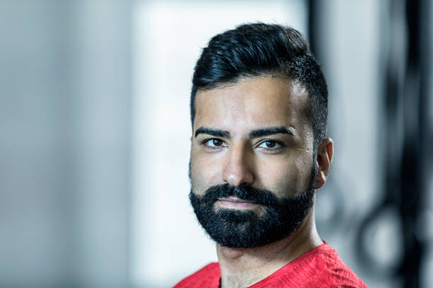 Headshot portrait of a handsome mid adult man of Iranian ethnicity. He is tan and well-groomed with neatly trimmed black hair and a thick, dark beard and mustache.