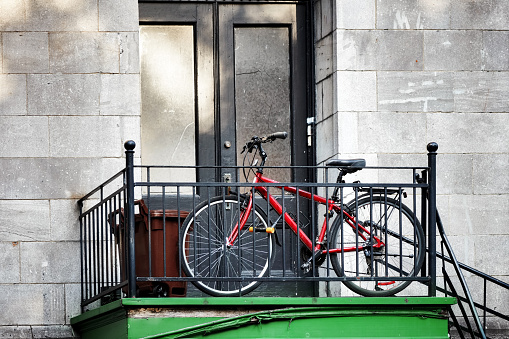 Red city bicycle parked in front of an old apartment door next to the staircase in Montreal, Canada