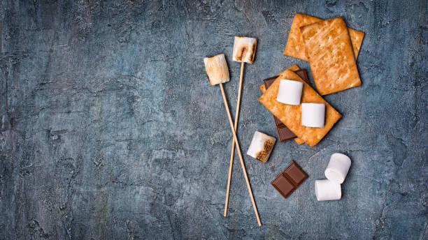 istock Top view on sticks with roasted on campfire marshmallow, crackers and chocolate as ingredients for s'mores 1085565358