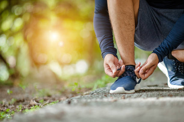 Man tying jogging shoes.A person running outdoors on a sunny day.Focus on a side view of two human hands reaching down to a athletic shoe.Young male jogger athlete training and doing workout outdoors hombre de atar los zapatos para correr. una persona corriendo al aire libre en un día soleado. se centran en una vista lateral de dos manos humanas llegan a un zapato atlético. atleta joven macho jogger formación y haciendo libre ejercicio