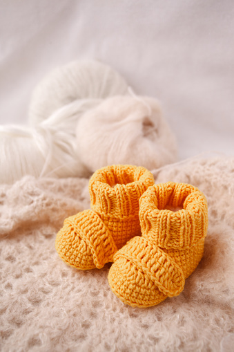 Children's yellow knitted booties on a light gentle background. The concept of expecting a child, motherhood, parenthood, the idea of a gift for a newborn
