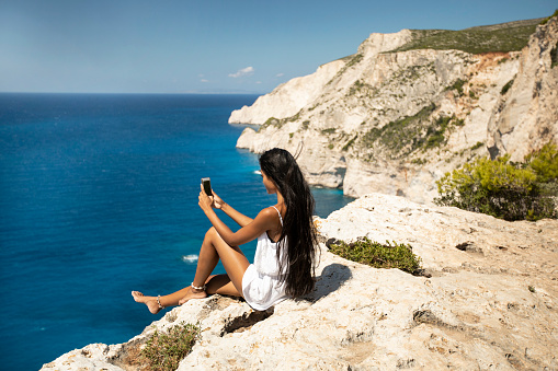 Beautiful woman sitting on cliff and using smart phone.