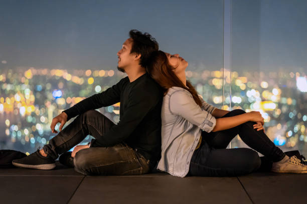 Romantic Couple Sitting on the rooftop from bangkok modern building at night time over the photo blurred of cityscape background, Lover and calentine holiday concept, low light Romantic Couple Sitting on the rooftop from bangkok modern building at night time over the photo blurred of cityscape background, Lover and calentine holiday concept, low light movie scene stock pictures, royalty-free photos & images