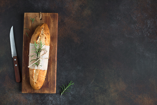 Fresh homemade bread with rosemary on rustic  background, top view, copy space. Sourdough mini baguette bread.