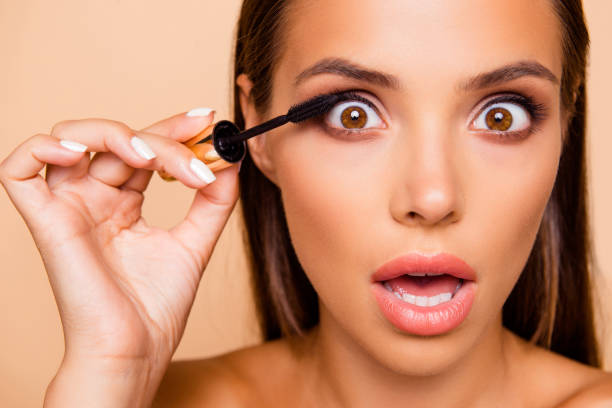 Cropped close up photo of careless carefree dreamy fun funky bru Cropped close up photo of careless carefree dreamy fun funky brunette hair lady with her shoulders she hold mascara in hand isolated on pastel beige background make open mouth staring eyes large eyes stock pictures, royalty-free photos & images