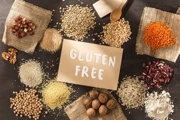 Gluten free flour and cereals millet, quinoa, corn bread, brown buckwheat, rice, bread and pasta with text gluten free in English language with spoon on wooden background, top view