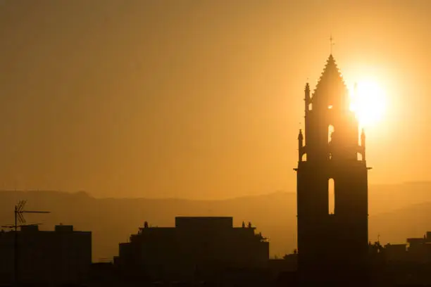 Church and belfry of Saint Peter at Golden hour in the city of Reus. Yellow sun and silhouettes